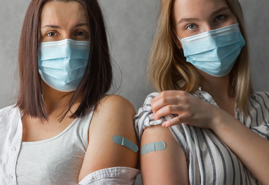 2 Frauen mit OP Maske und Pflaster am Oberarm